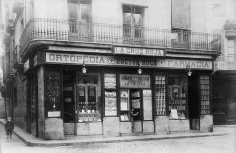Establiment Ortopèdia-farmàcia Doctor Roca a la plaça de l'Oli. Façana de l'establiment on apareix el rètol de la farmàcia i el de l'administració de loteria n 2. 1935-1940