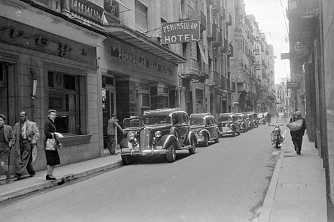 Taxis estacionats davant l'hotel Peninsular, al carrer Nou. A l'esquerra s'observa el restaurant Savoy. 1957