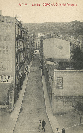 El carrer Nou a lencreuament amb la Gran Via de Jaume I. En primer terme a la dreta, un cartell publicitari de la marca de màquines de cosir Singer. 1902