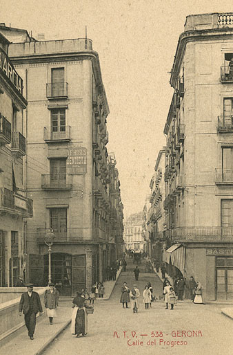 El carrer Nou des del pont de Pedra. En primer terme, al terrat de l'edifici de l'esquerra, publicitat del fotògraf Antoni Garcia situada en el terrat del mateix edifici. A l'edifici del costat, la clínica dental A.F. Roses. 1904