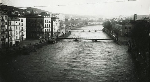 Vista des d'un punt elevat d'una crescuda del riu Onyar. Al centre, el pont del Pes de la Palla i el pont del Carme. A l'esquerra, el carrer del Carme i a la dreta, el convent del Mínims. 1913-1920