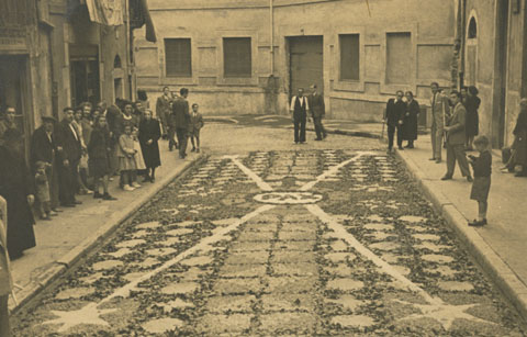 Diada de Corpus al carrer del Perill. S'observa la gent contemplant les catifes de flors des de les voreres del carrer. 1940